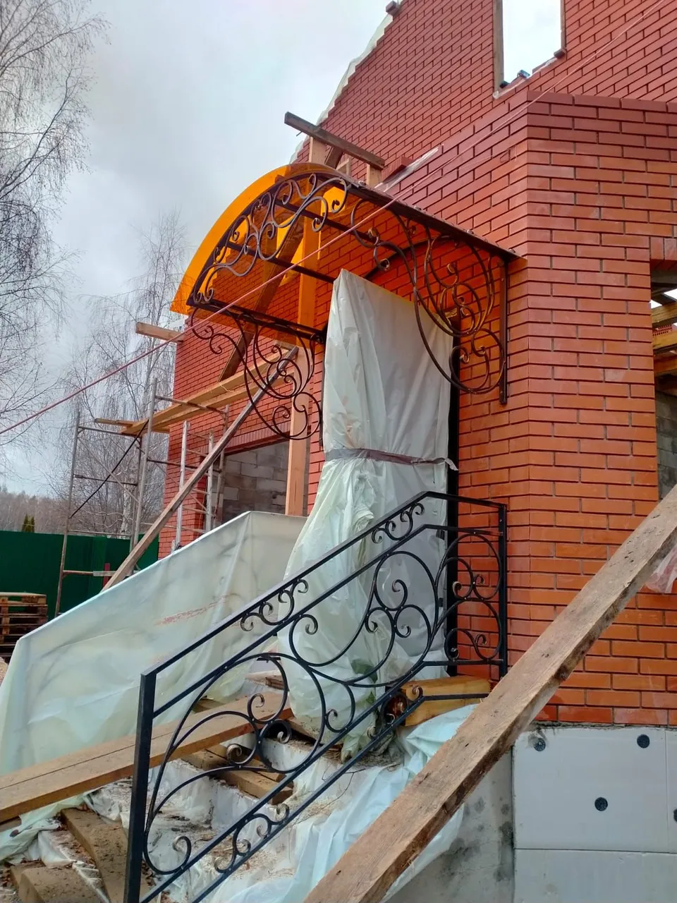 Арочный козырёк над входом на кованых консолях и перила крыльца с завитками