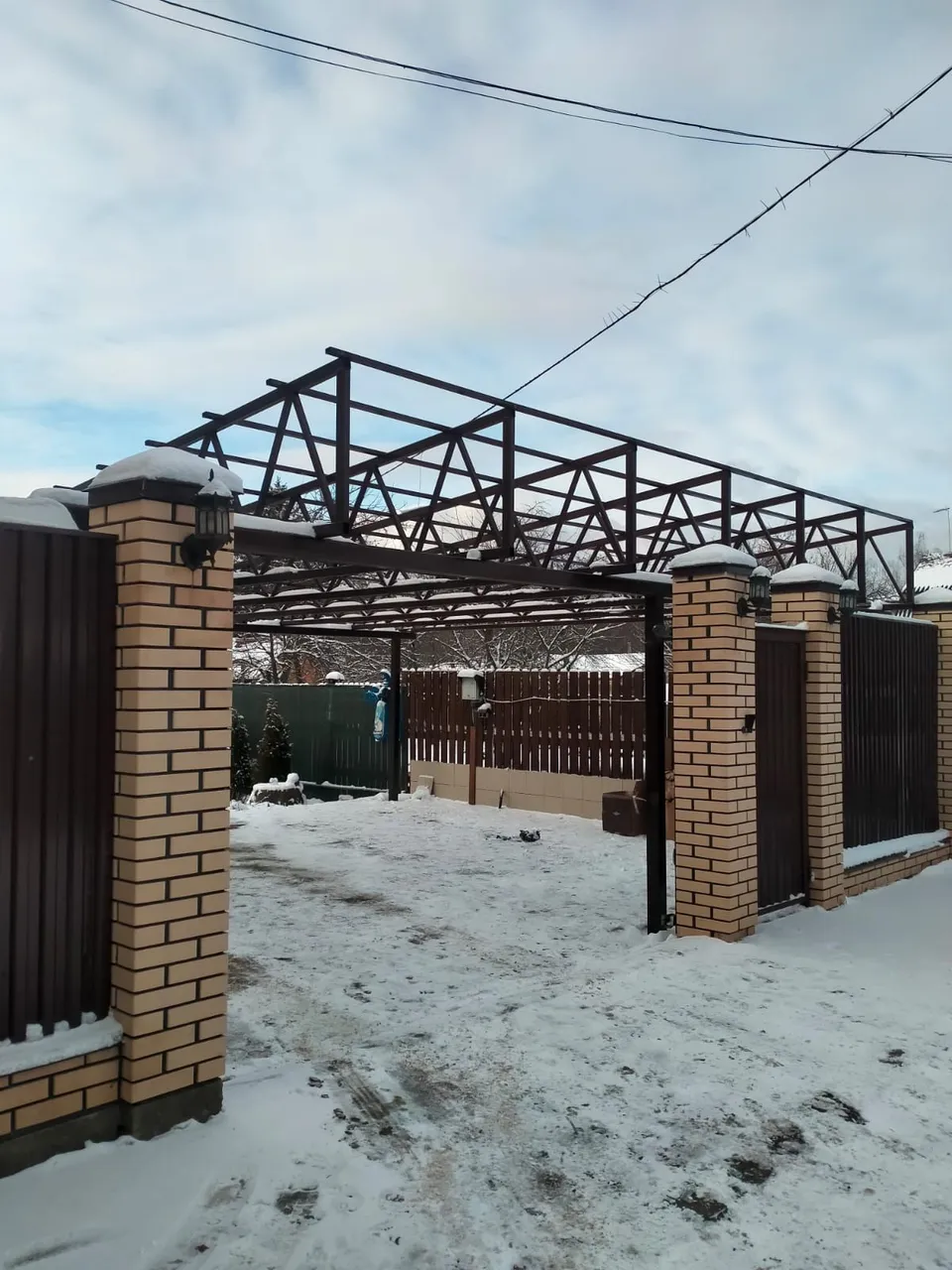 Каркас плоского навеса на фермах между кирпичными столбами над въездом